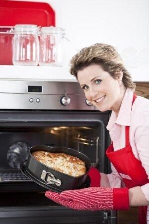 schöne Frau schiebt Herzformkuchen in Ofen